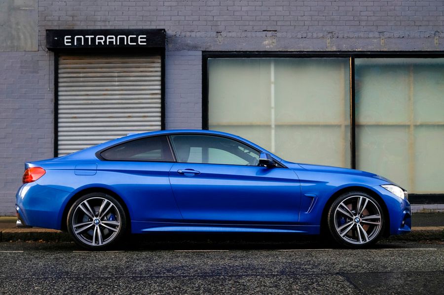 BMW 440i M Sport bleue, vue de profil, à l'arrêt le long d'un trottoir